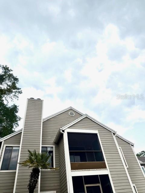 A low-angle exterior view of a two-story house with light gray siding and a screened balcony — 549 SUN RIDGE PLACE UNIT 201, ALTAMONTE SPRINGS, FL