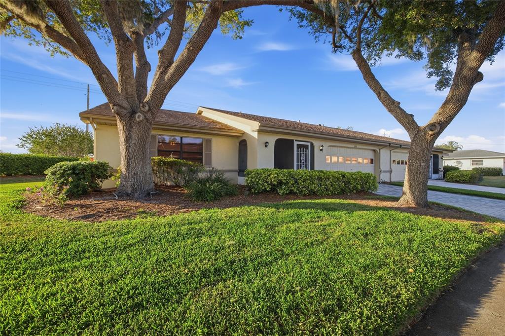 A single-story house with a beige exterior, a two-car garage, and two large oak trees — 2331 LANCASTER DRIVE, SUN CITY CENTER, FL