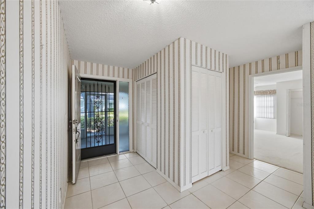 An entryway with tiled floors, striped wallpaper, and two sets of white louvered closet doors — 2331 LANCASTER DRIVE, SUN CITY CENTER, FL