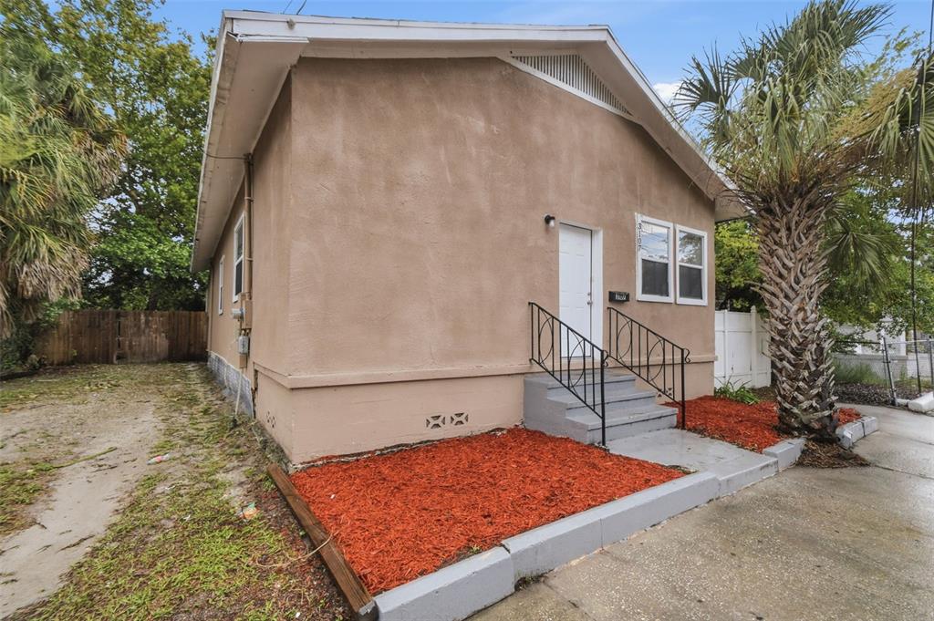 A tan stucco house features a white front door, black railings, and red mulch landscaping — 3107 N 16TH STREET, TAMPA, FL