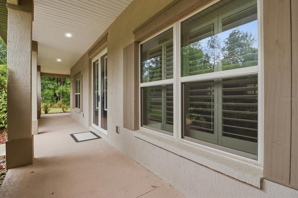 A covered patio features a beige stucco wall, large windows with shutters, and glass doors — 2463 W AXELWOOD DRIVE, BEVERLY HILLS, FL