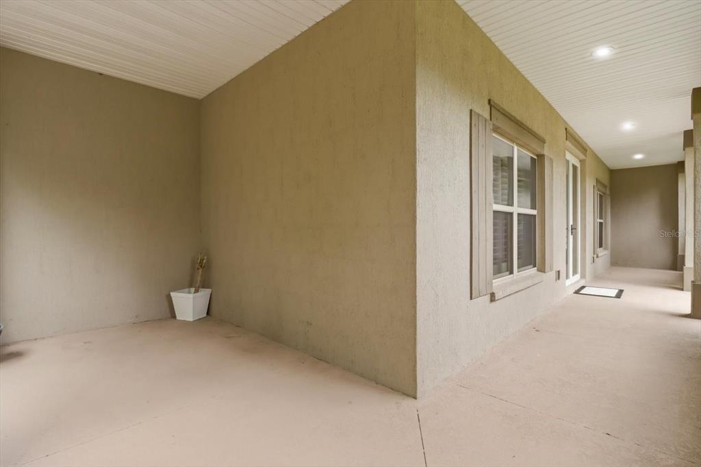 A covered outdoor porch with tan stucco walls, a window with shutters, and recessed lighting — 2463 W AXELWOOD DRIVE, BEVERLY HILLS, FL