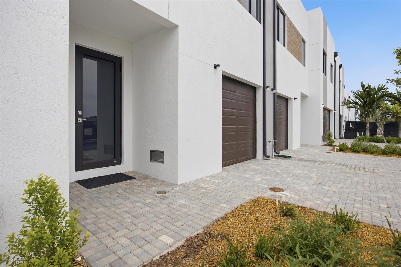 A row of modern white townhouses features dark garage doors and front entryways with paver driveways — 1546 NW 1st Avenue, Pompano Beach FL 33060, POMPANO BEACH, FL