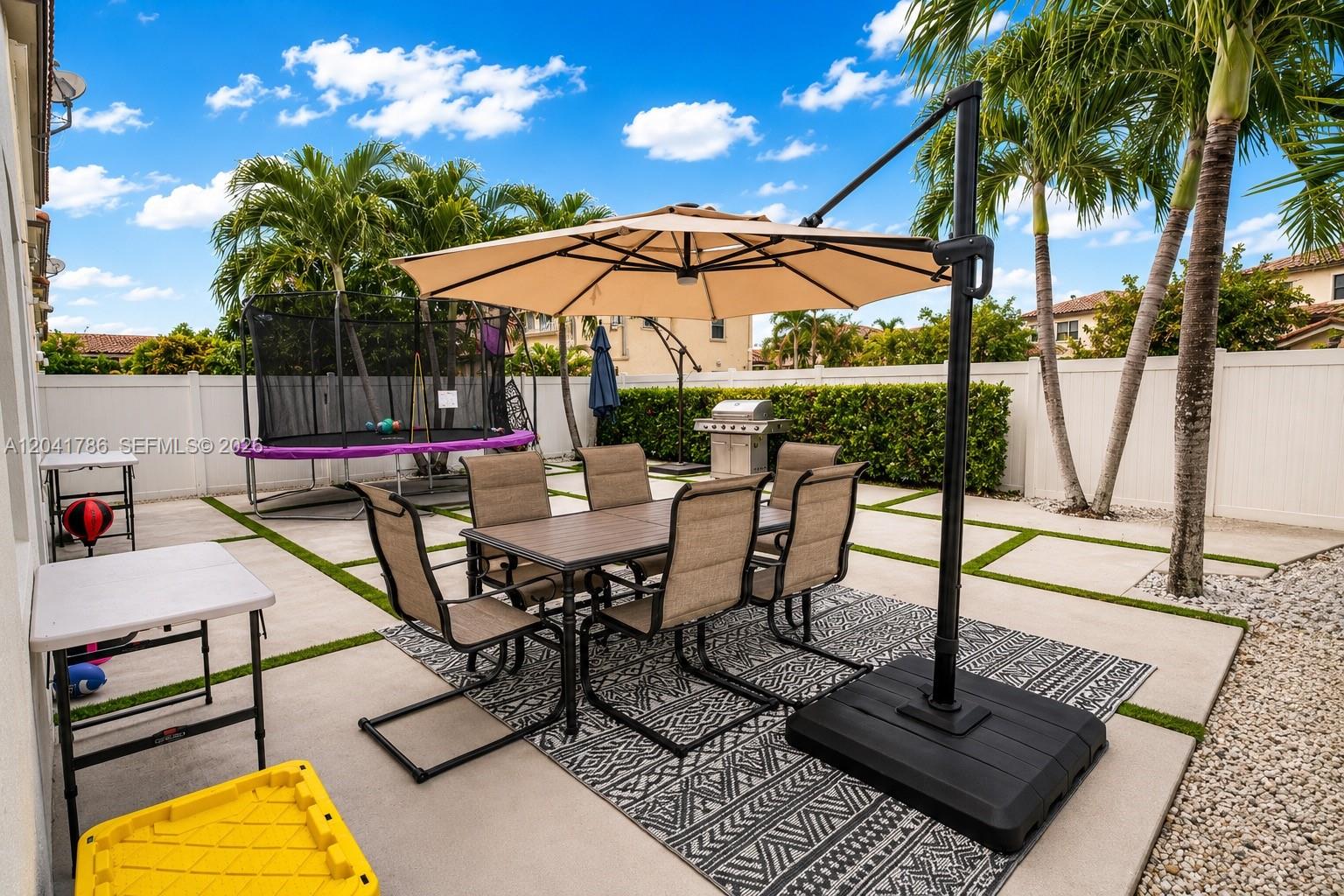 A patio features a dining set with an umbrella, a trampoline, and a grill — 8821 W 34th Ct, Hialeah FL 33018, HIALEAH, FL