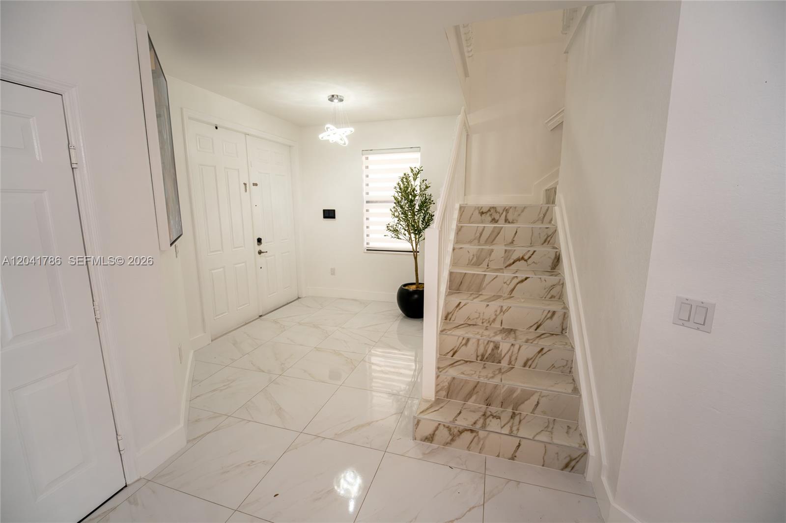 An entryway features white marble-look tile flooring, a staircase with matching treads, and a front door — 8821 W 34th Ct, Hialeah FL 33018, HIALEAH, FL