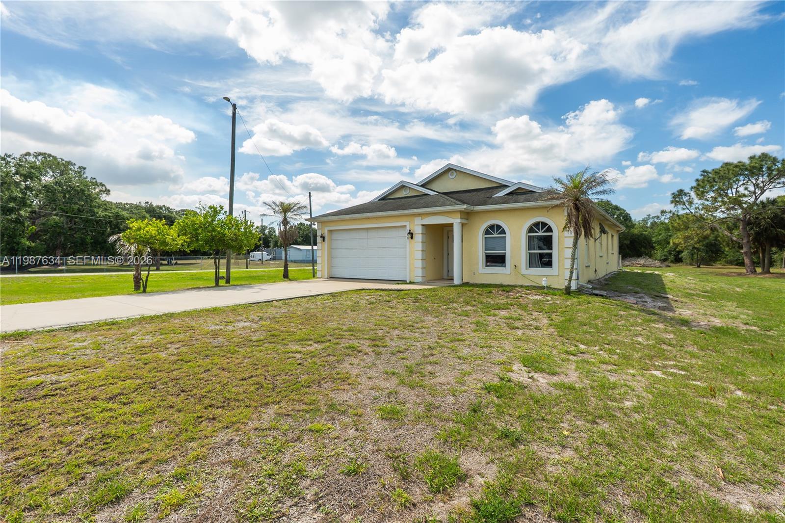 A yellow single-story house with a two-car garage sits on a large, grassy lot — 166 Pine Cone Ave, Clewiston FL 33440, CLEWISTON, FL