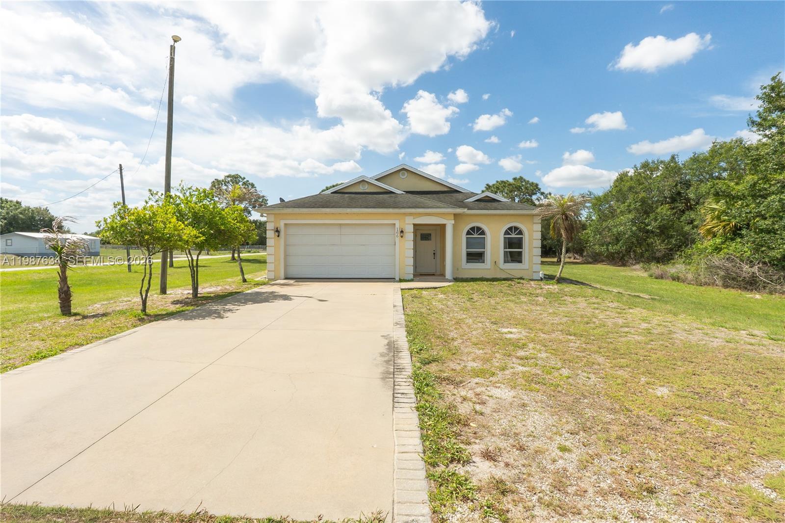 A single-story house with a beige exterior, a two-car garage, and a concrete driveway — 166 Pine Cone Ave, Clewiston FL 33440, CLEWISTON, FL