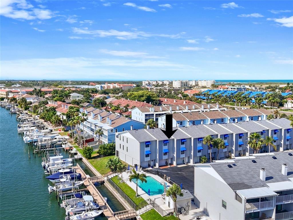 An aerial view shows a multi-story residential building with blue awnings beside a boat canal — 745 PINELLAS BAYWAY S UNIT 202, TIERRA VERDE, FL