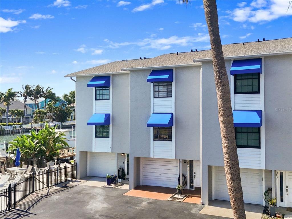 Exterior view of a three-story townhouse complex with blue awnings and attached garages — 745 PINELLAS BAYWAY S UNIT 202, TIERRA VERDE, FL
