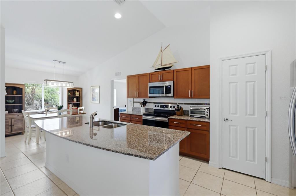 A kitchen features wood cabinets, granite countertops, a central island, and a dining area nearby — 150 BAYTREE DRIVE, ROTONDA WEST, FL