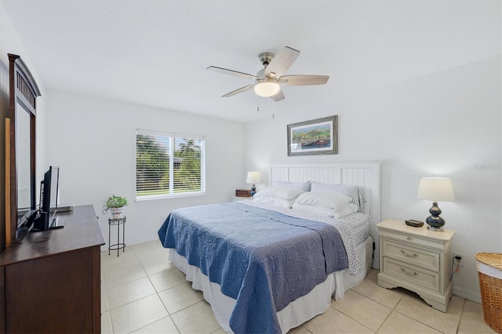 A bedroom features a bed with a blue quilt, a ceiling fan, and tile flooring — 150 BAYTREE DRIVE, ROTONDA WEST, FL