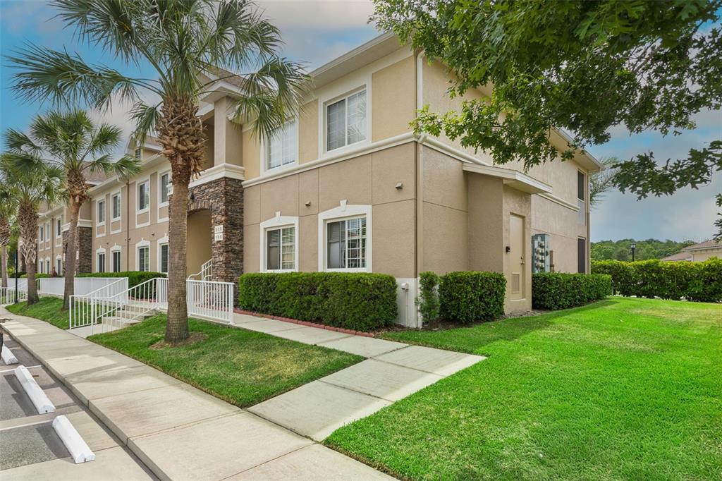 A two-story apartment building with tan stucco walls, stone accents, and a landscaped lawn — 1195 GODAVARI WAY UNIT 105, WESLEY CHAPEL, FL