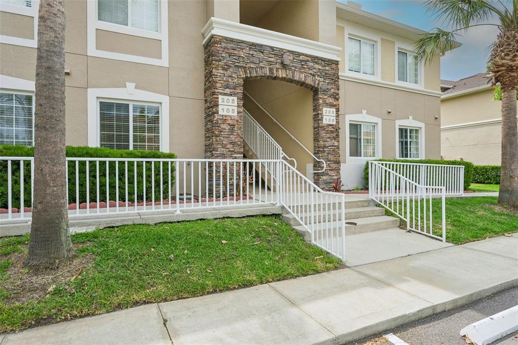 The exterior of a multi-story apartment building features a stone-accented entrance with stairs — 1195 GODAVARI WAY UNIT 105, WESLEY CHAPEL, FL