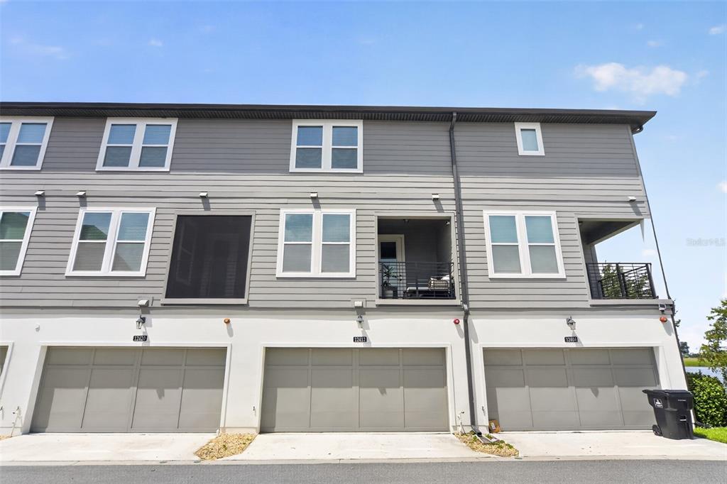 A three-story townhouse exterior features gray horizontal siding, white trim, and three garage doors — 12412 KOSHIBA ALLEY, ORLANDO, FL