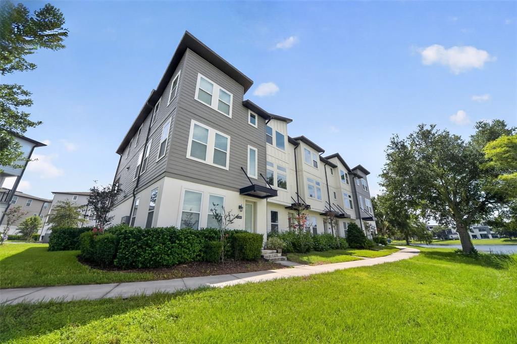 A multi-story townhouse exterior with gray and white siding sits beside a grassy lawn — 12412 KOSHIBA ALLEY, ORLANDO, FL