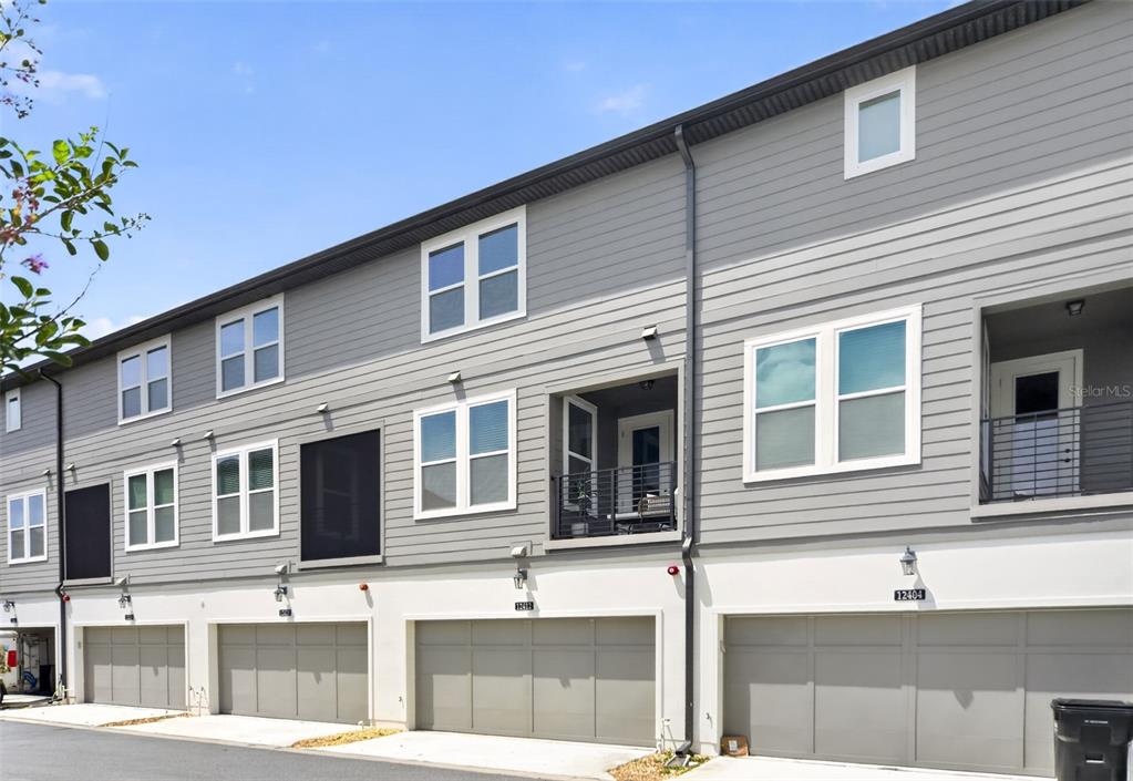 A row of gray townhouses with multiple garage doors and balconies under a blue sky — 12412 KOSHIBA ALLEY, ORLANDO, FL