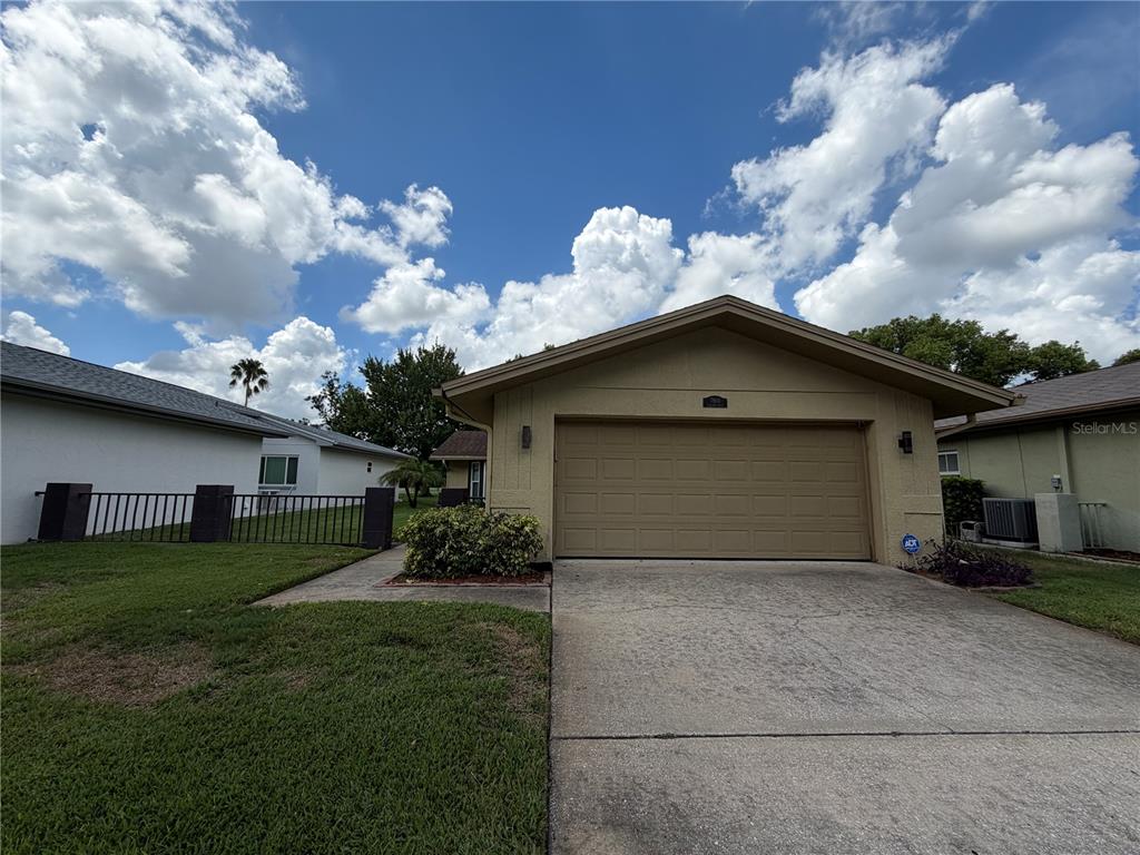 A tan single-story house with a two-car garage and a concrete driveway under a cloudy sky — 7800 FAIRLAWN DRIVE, HUDSON, FL