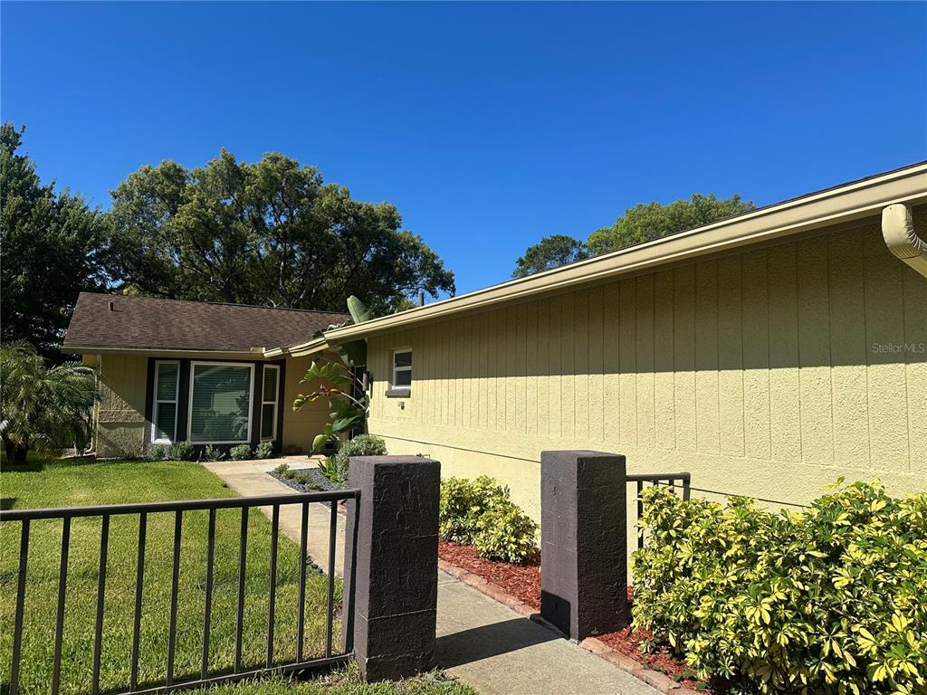 A yellow house exterior features a walkway leading to the front entrance behind a fence — 7800 FAIRLAWN DRIVE, HUDSON, FL