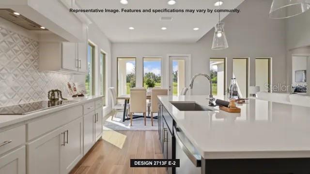 A modern kitchen features white cabinetry, a large quartz island, and a dining area beyond — 13062 CAMELOT LANE, PUNTA GORDA, FL