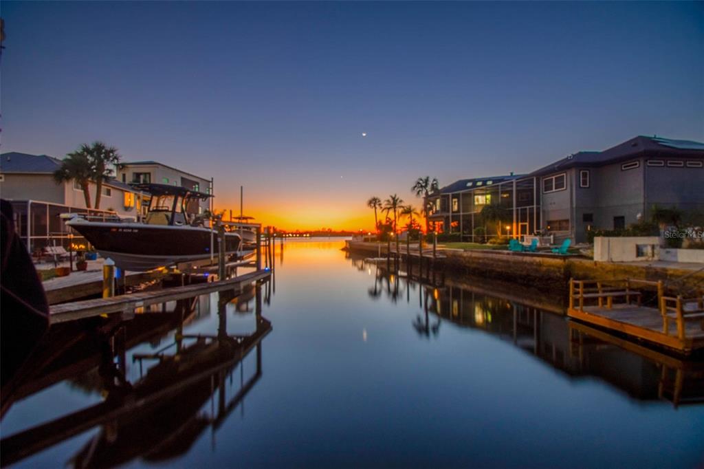 A canal view at sunset featuring houses, boat docks, and a boat on a lift — 8034 BRIGHTON DRIVE, PORT RICHEY, FL