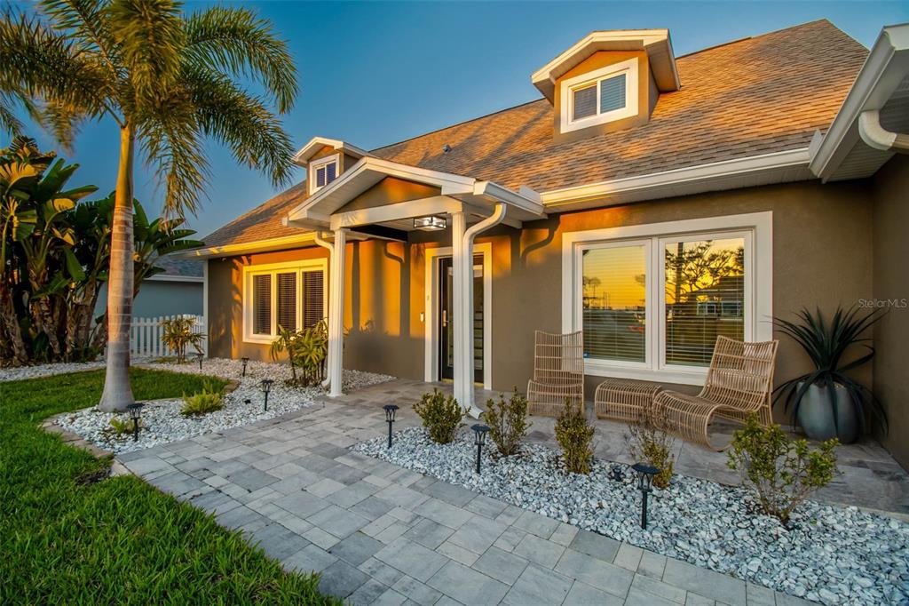 A tan house exterior features a stone walkway, white gravel landscaping, and a palm tree — 8034 BRIGHTON DRIVE, PORT RICHEY, FL