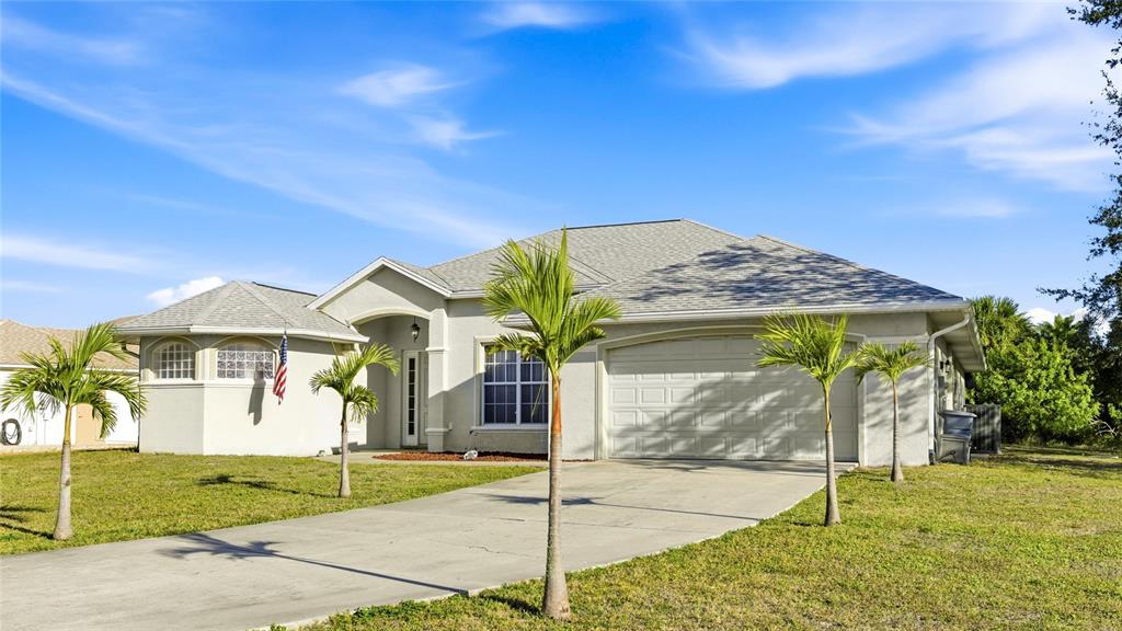 A single-story suburban house with a concrete driveway, palm trees, and an American flag — 17220 HORIZON LANE, PORT CHARLOTTE, FL