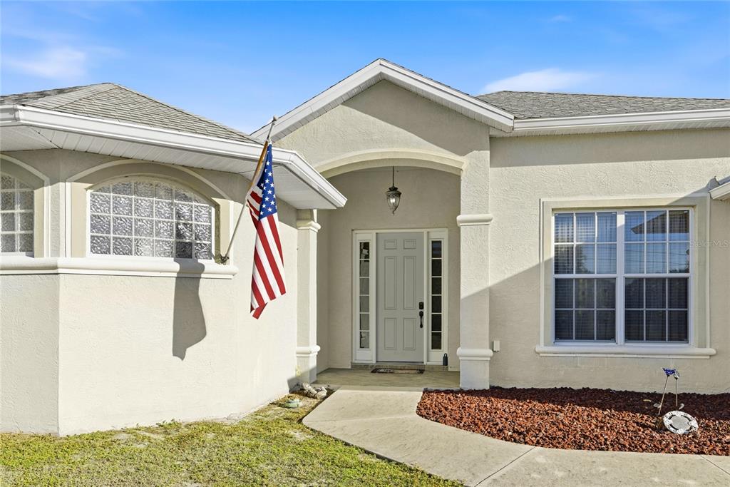 A beige stucco house exterior features a front entrance with an American flag — 17220 HORIZON LANE, PORT CHARLOTTE, FL