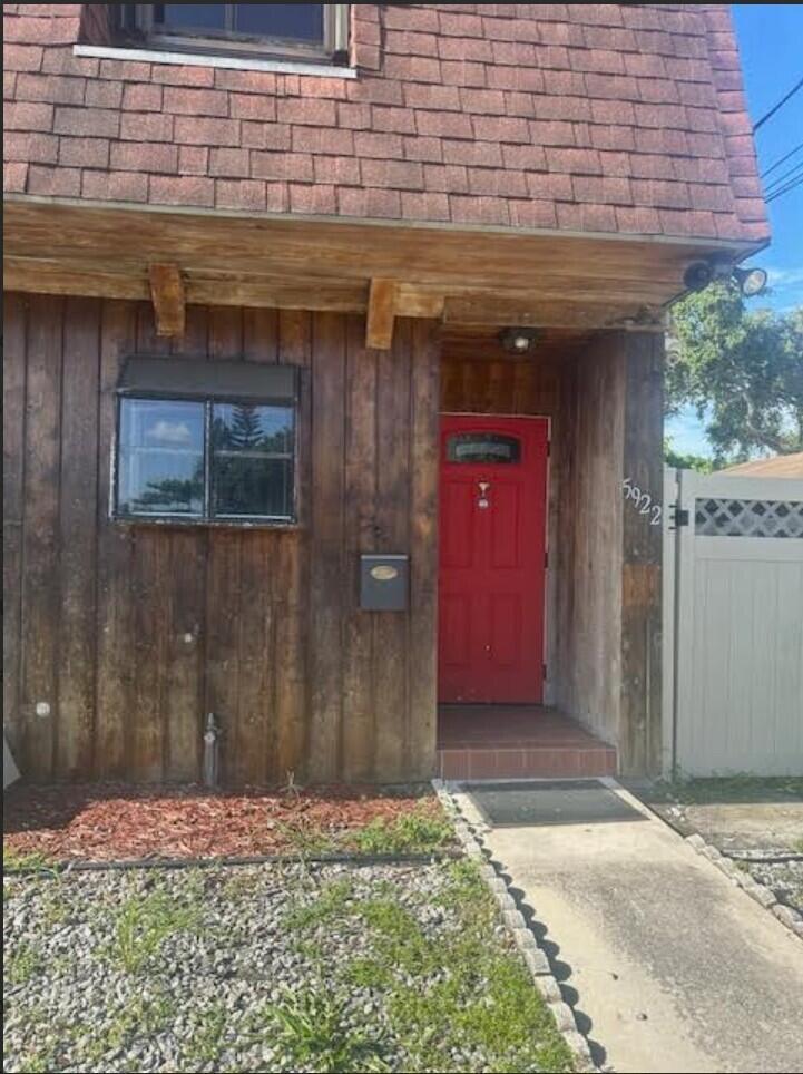 The exterior of a house features vertical wood siding, a red door, and shingled roofing — 5922 Thomas Street, Hollywood FL 33021, HOLLYWOOD, FL