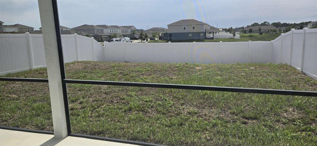 A view of a fenced backyard with sparse grass from a screened-in patio — 1564 EUCALYPTUS WAY, DAVENPORT, FL