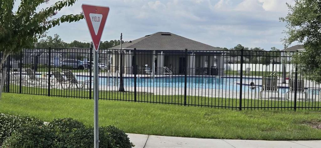 A fenced community swimming pool with lounge chairs and a clubhouse building in the background — 1564 EUCALYPTUS WAY, DAVENPORT, FL
