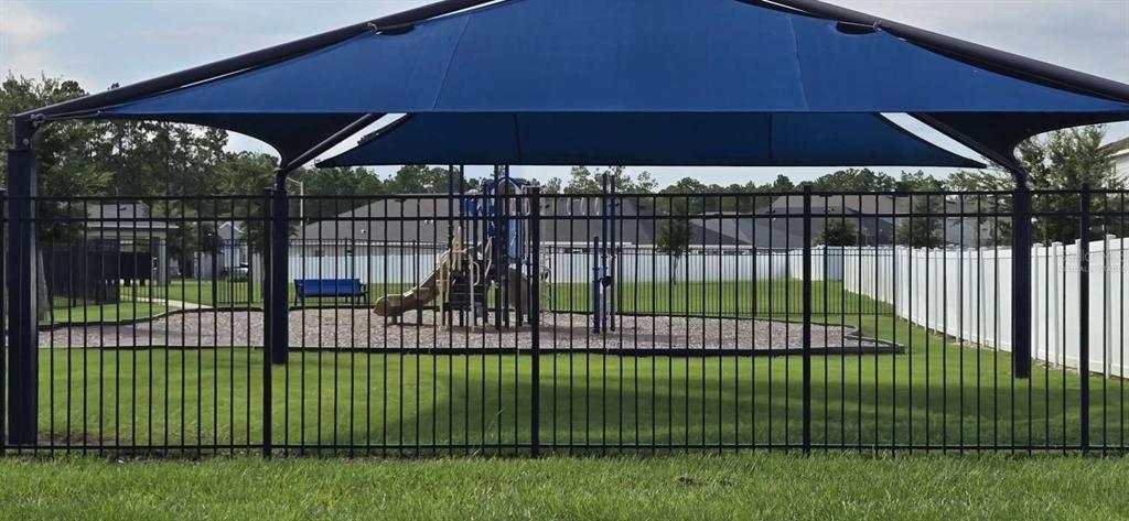 A fenced playground area features a blue shade canopy over a small play structure — 1564 EUCALYPTUS WAY, DAVENPORT, FL