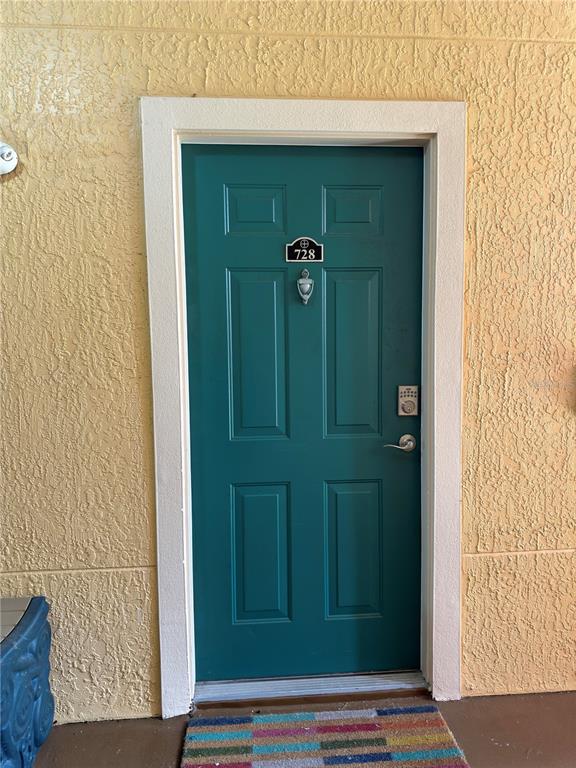 A teal front door with a silver knocker and keypad lock sits in a yellow wall — 2715 VIA CAPRI UNIT 728, CLEARWATER, FL