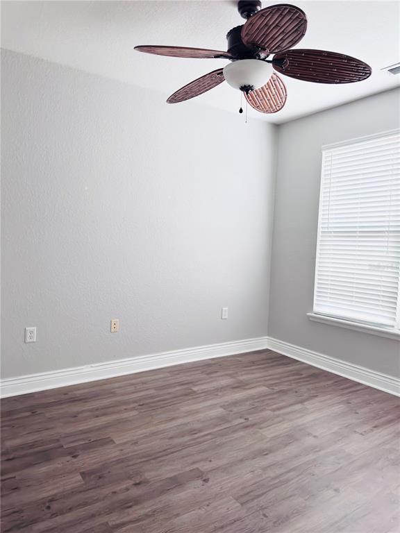 An empty room features light gray walls, wood-look flooring, a ceiling fan, and a window — 2715 VIA CAPRI UNIT 728, CLEARWATER, FL
