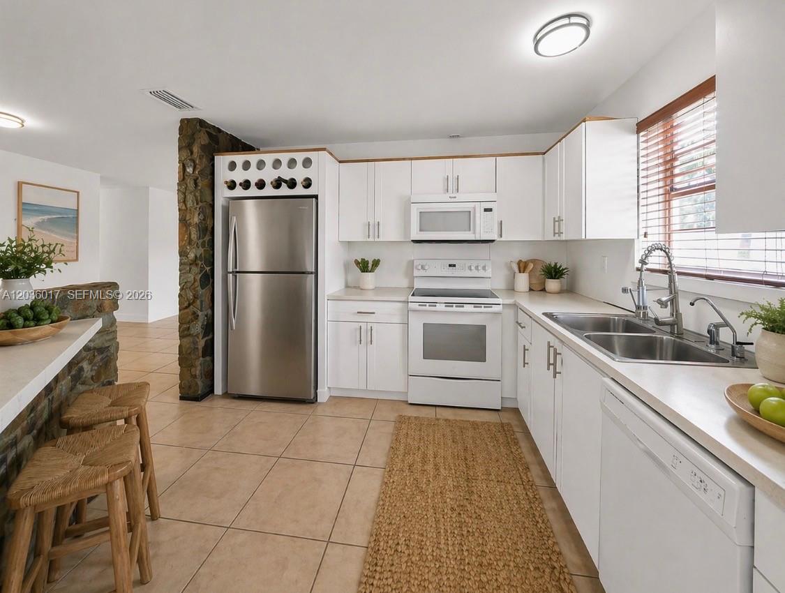 A kitchen features white cabinets, stainless steel appliances, a stone accent wall, and tile flooring — 8241 SW 12th Ter, Miami FL 33144, MIAMI, FL