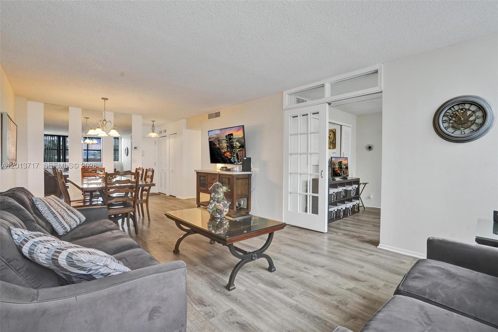 A living room features gray sofas, a glass coffee table, and French doors leading inside — 2017 S Ocean Dr # 205, Hallandale Beach FL 33009, HALLANDALE BEACH, FL
