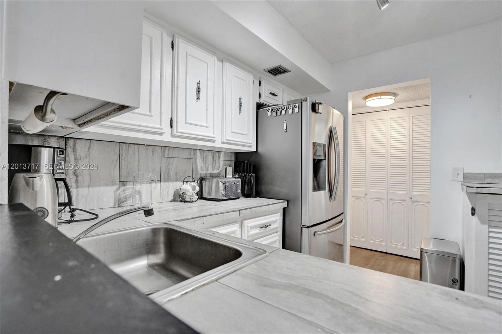 A kitchen features white cabinets, stainless steel appliances, and a gray tiled backsplash — 2017 S Ocean Dr # 205, Hallandale Beach FL 33009, HALLANDALE BEACH, FL