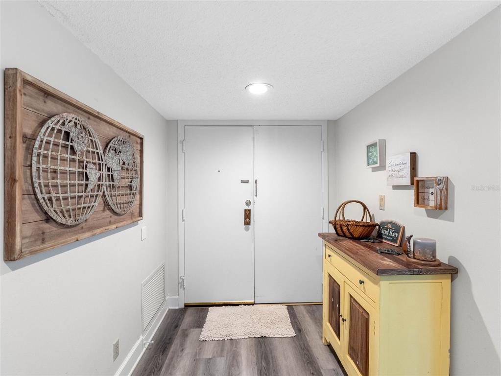 An entryway features light gray walls, wood-look flooring, a yellow cabinet, and a world map wall art — 1460 GULF BOULEVARD UNIT 308, CLEARWATER BEACH, FL