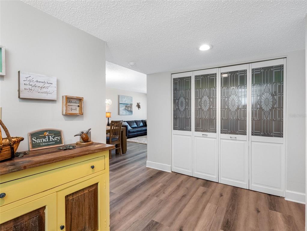 A hallway features wood-look flooring, a yellow cabinet, and white closet doors with decorative glass — 1460 GULF BOULEVARD UNIT 308, CLEARWATER BEACH, FL