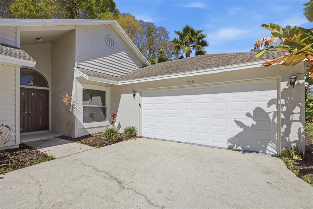 A single-story house exterior features a white garage, a front entrance, and a concrete driveway — 812 CRESTRIDGE DRIVE, TARPON SPRINGS, FL