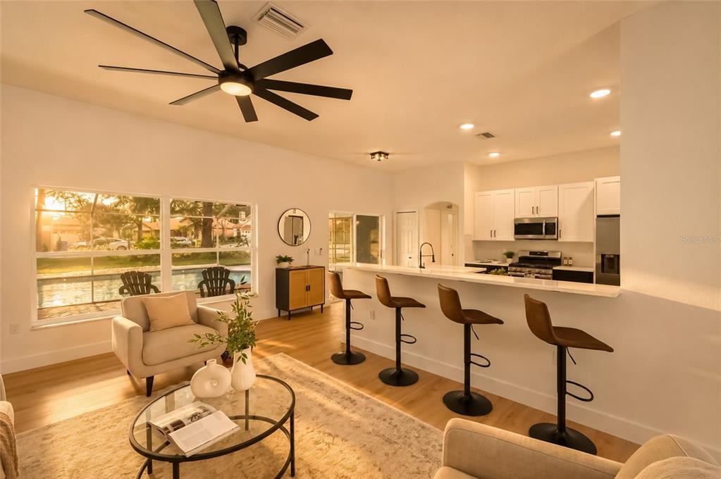 An open-concept living room and kitchen featuring a breakfast bar, ceiling fan, and pool view — 10117 WHISPER POINTE DRIVE, TAMPA, FL
