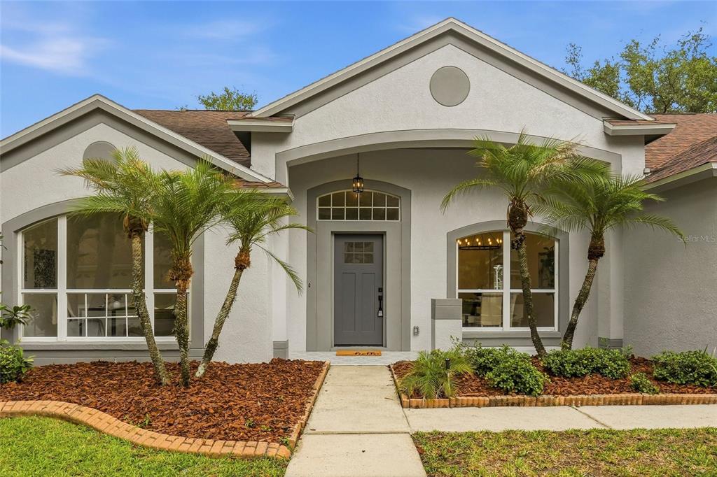 A single-story house exterior with a gray front door, arched windows, and two palm trees — 10117 WHISPER POINTE DRIVE, TAMPA, FL