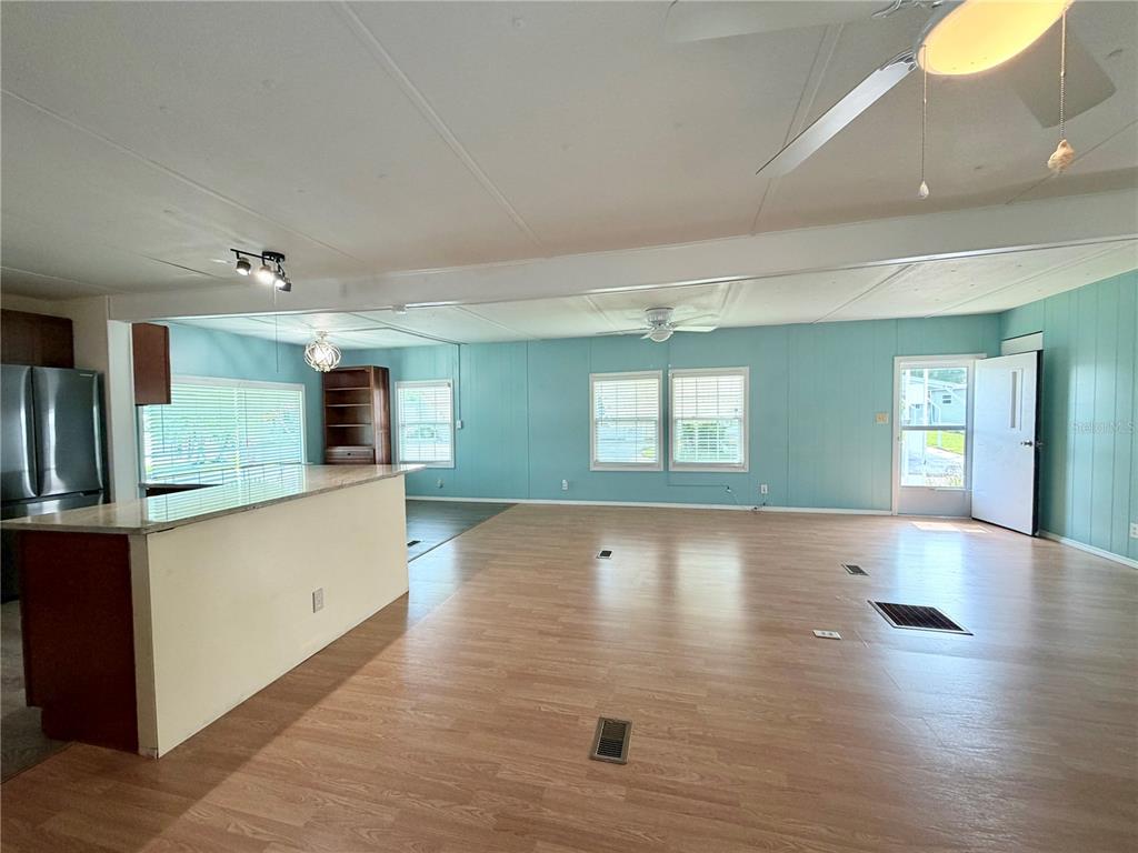 An open-concept living area features light wood flooring, blue walls, and a kitchen island — 9790 66TH STREET N UNIT 100, PINELLAS PARK, FL