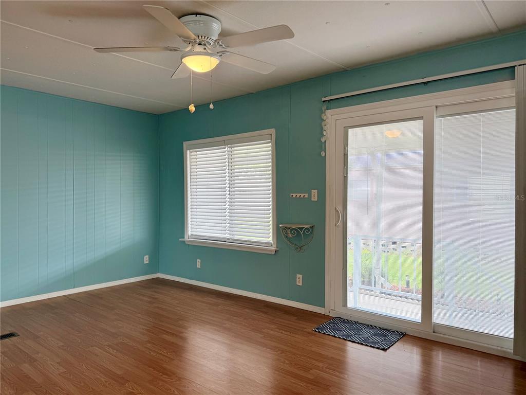 A room with light blue walls, wood-look flooring, a ceiling fan, and sliding glass doors — 9790 66TH STREET N UNIT 100, PINELLAS PARK, FL