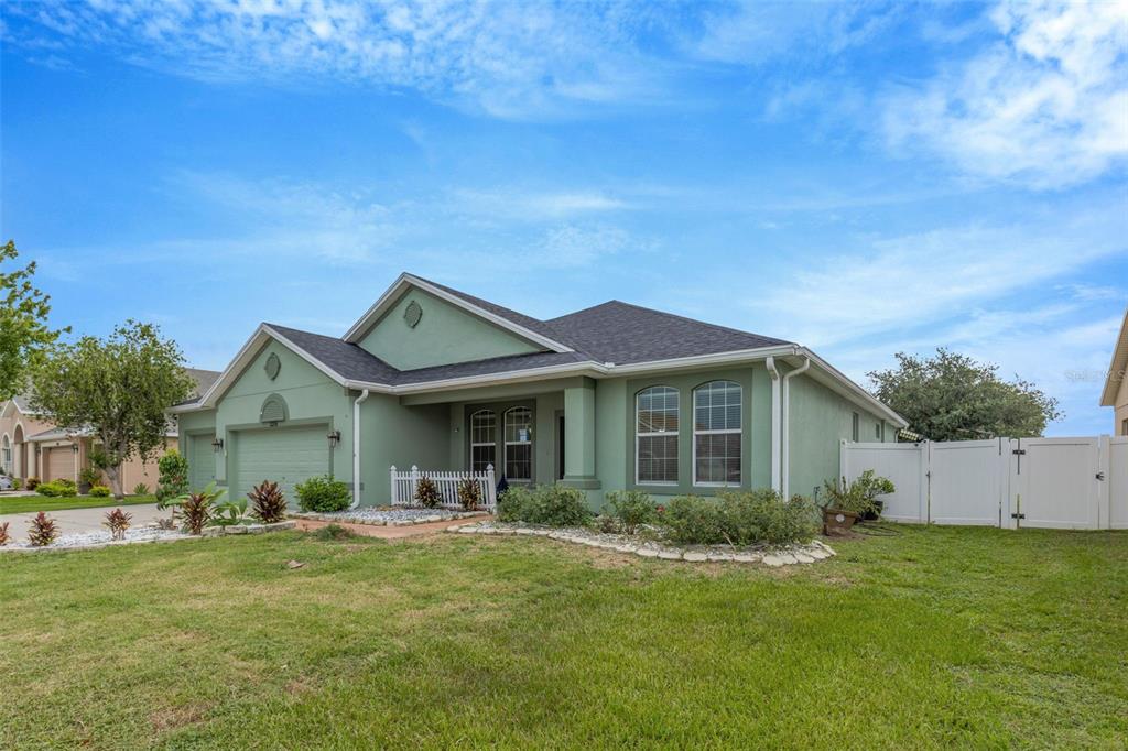 A single-story green stucco house with a two-car garage and a white vinyl fence — 2206 VIA CORTONA STREET, PLANT CITY, FL