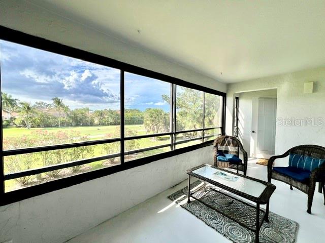 A sunroom features large windows overlooking a green landscape, wicker furniture, and a glass-topped table — 801 ISLAMORADA BOULEVARD UNIT 22B, PUNTA GORDA, FL