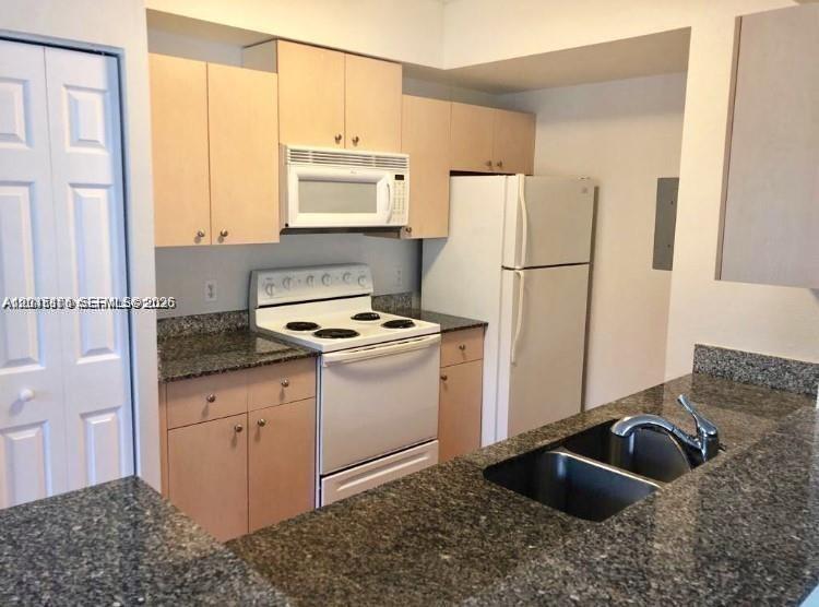 A kitchen features light wood cabinets, granite countertops, a white stove, and a white refrigerator — 2493 Centergate Dr # 204, Miramar FL 33025, MIRAMAR, FL