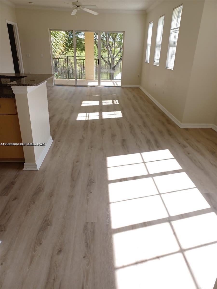 An empty living area features light wood-look flooring, large windows, and a sliding glass door — 2493 Centergate Dr # 204, Miramar FL 33025, MIRAMAR, FL