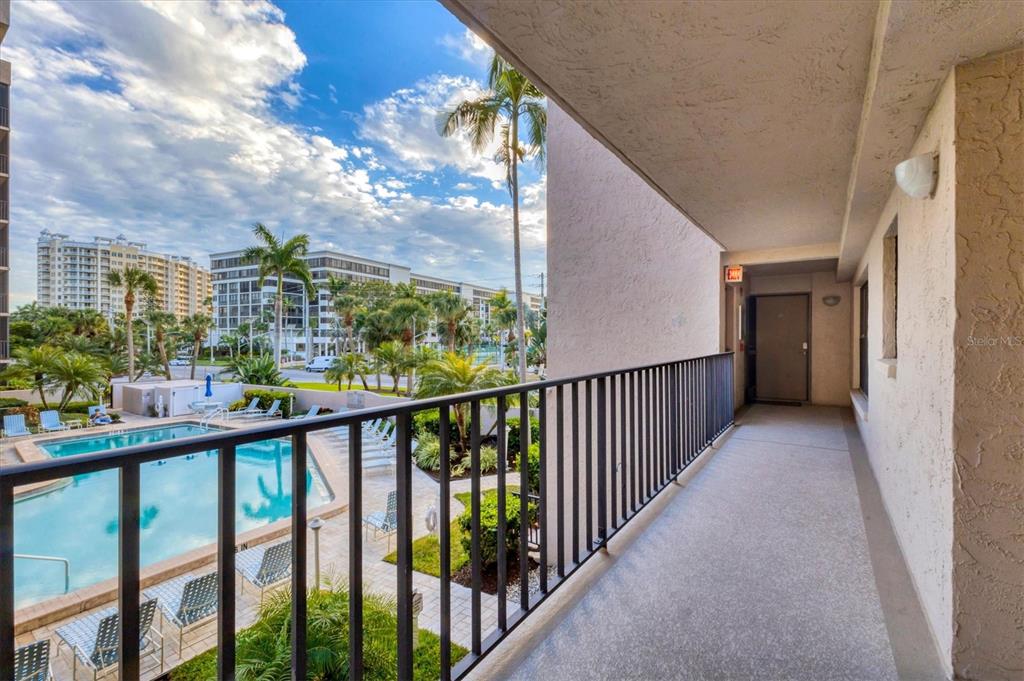 An outdoor balcony overlooks a swimming pool and palm trees under a blue sky — 1001 BENJAMIN FRANKLIN DRIVE UNIT 201, SARASOTA, FL