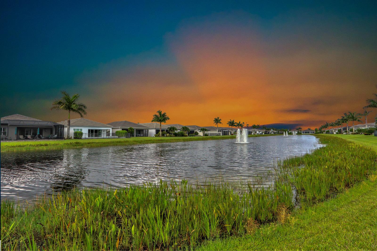 A pond with fountains sits in front of a row of houses at sunset — 9939 Great Barrier Trail, Boynton Beach FL 33473, BOYNTON BEACH, FL