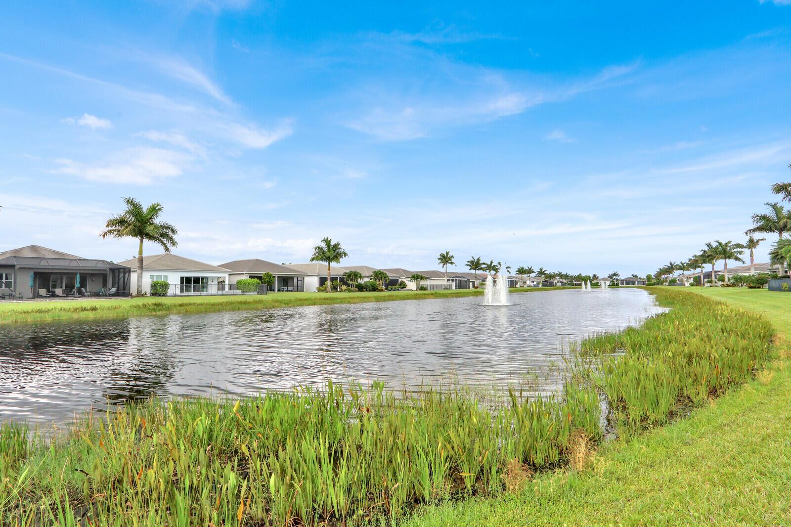 A pond with fountains sits in front of a row of houses and palm trees — 9939 Great Barrier Trail, Boynton Beach FL 33473, BOYNTON BEACH, FL